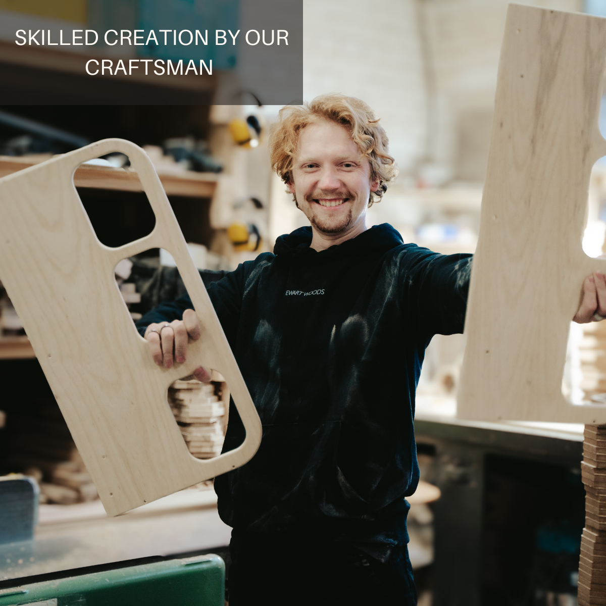 A smiling craftsman in a workshop holds two wooden pieces of the toy bus frame, showcasing his skilled craftsmanship.
