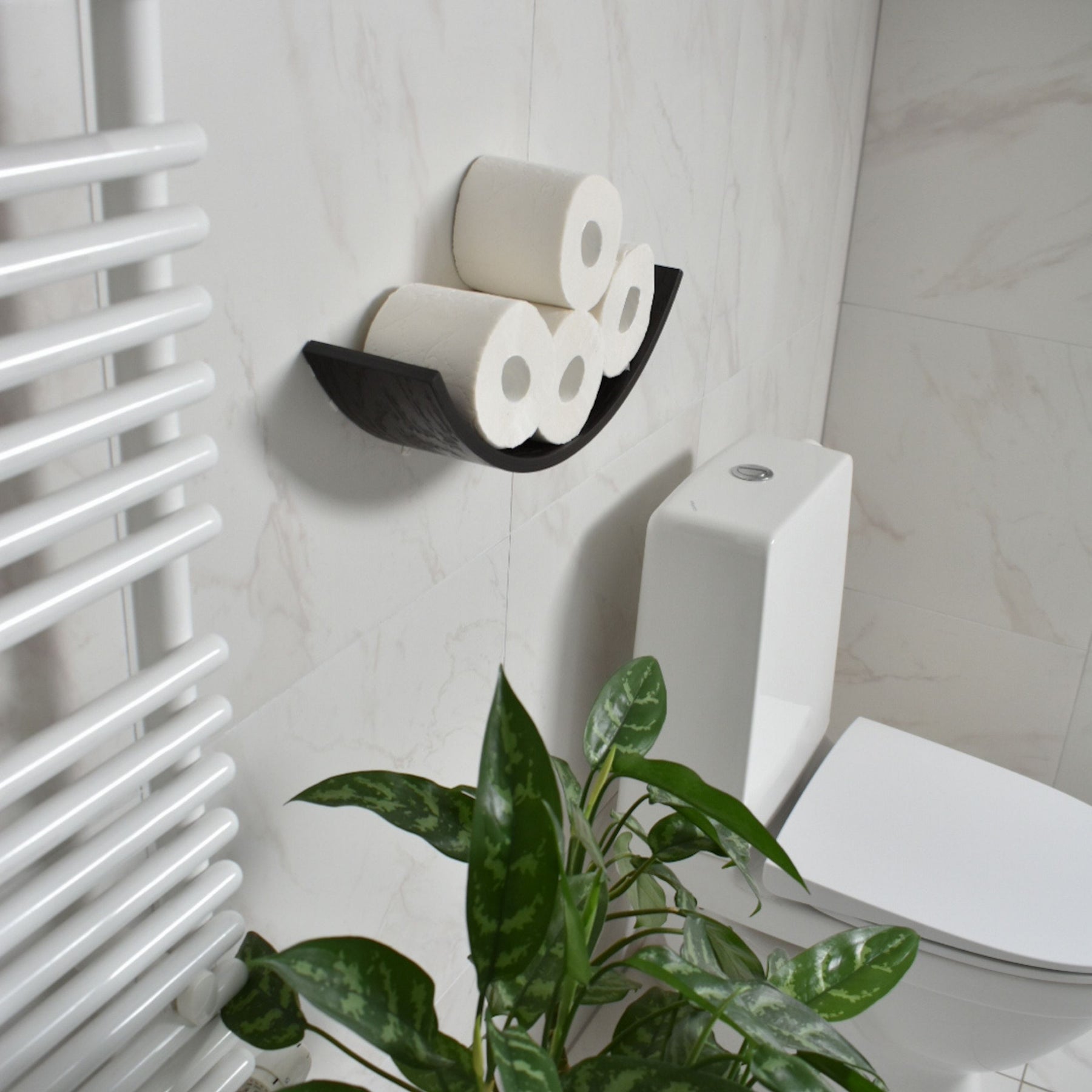 Space-saving dark brown toilet roll holder with a hidden mounting system on a bathroom wall near the toilet, with greenery on the side.