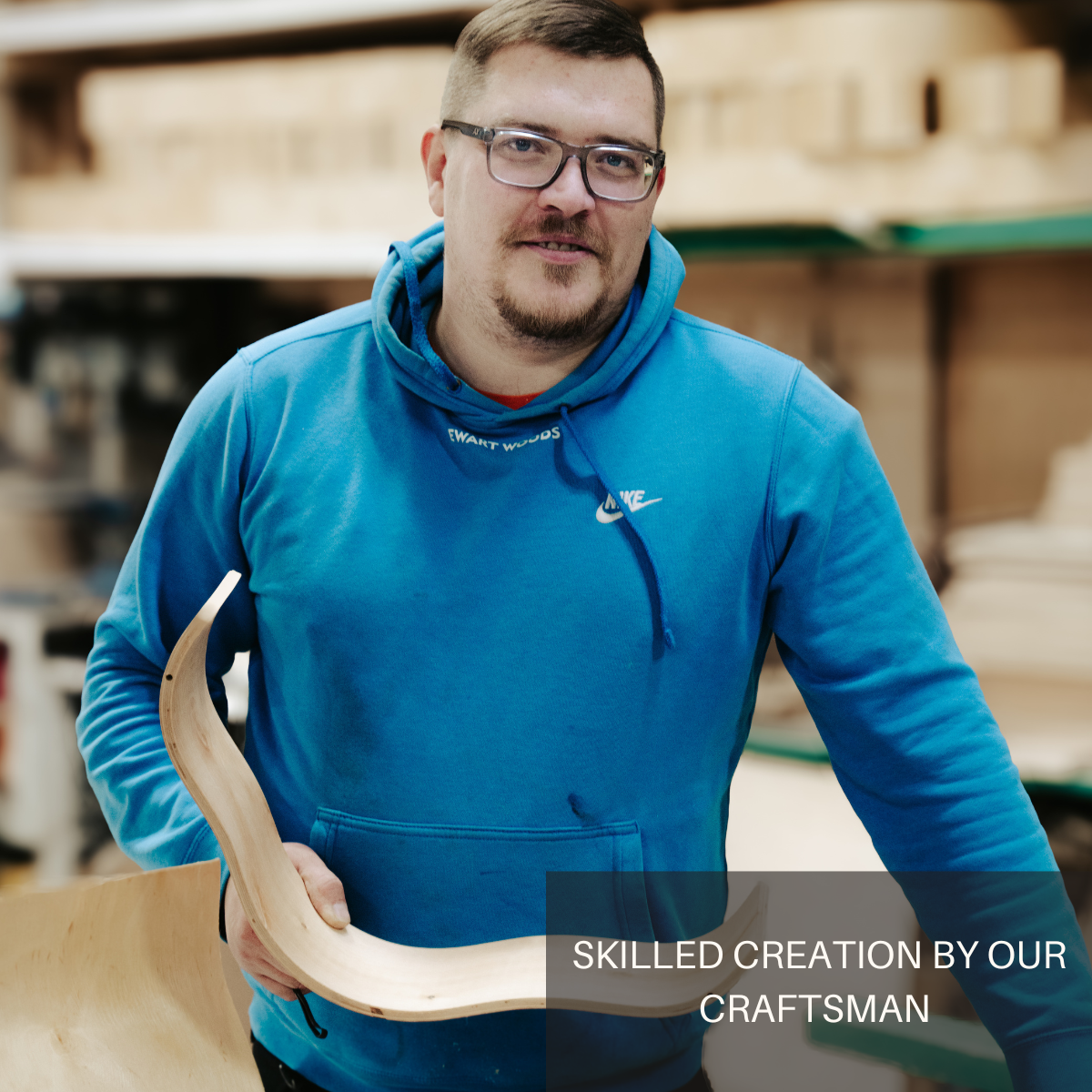Craftsman holding an ash wooden shelf with a curved design, showcasing skilled craftsmanship in the workshop. The image includes the text SKILLED CREATION BY OUR CRAFTSMAN at the bottom.