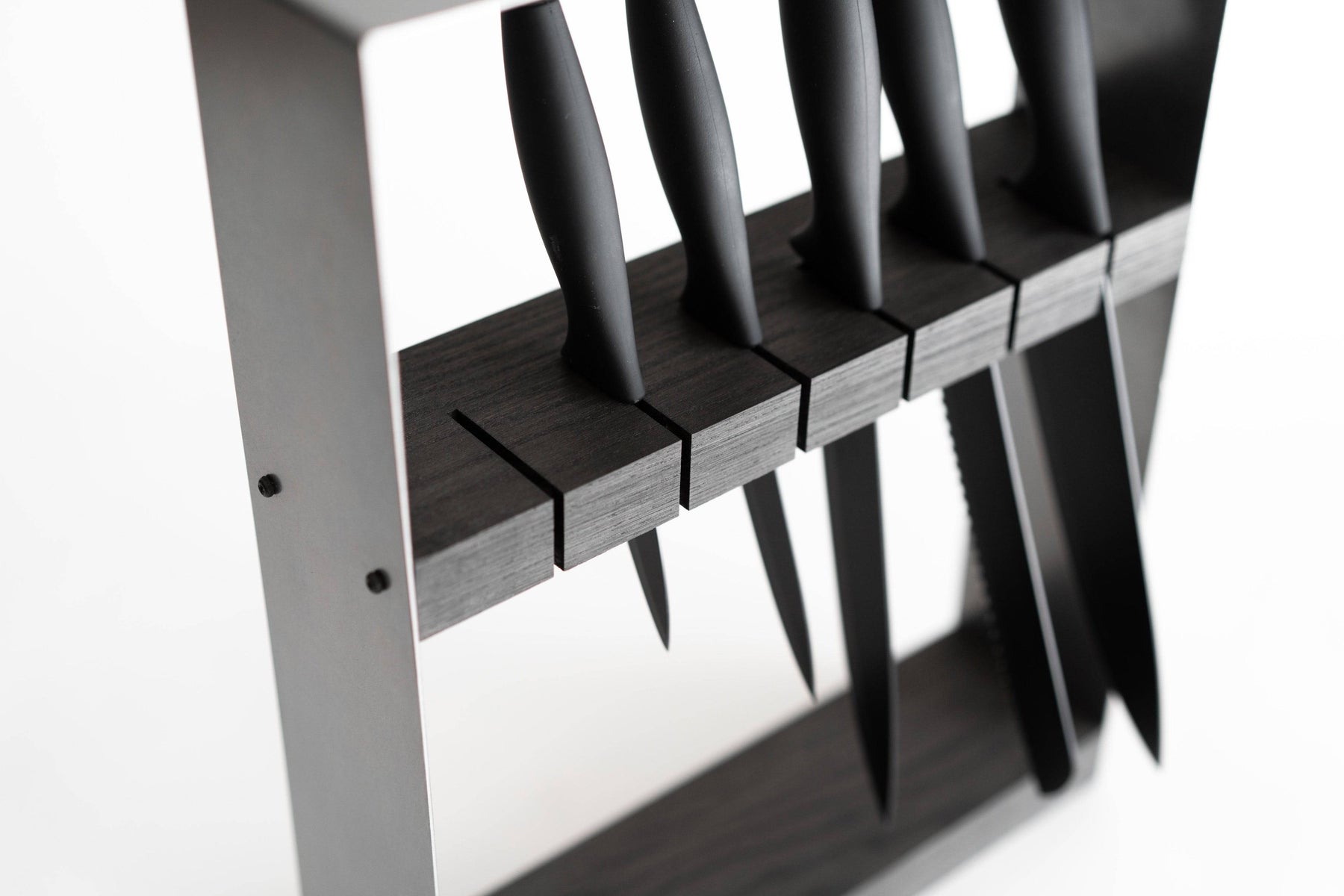 Angled view of a sleek, modern knife block featuring a black metal frame and dark wooden insert, holding six black-handled knives in evenly spaced horizontal slots.