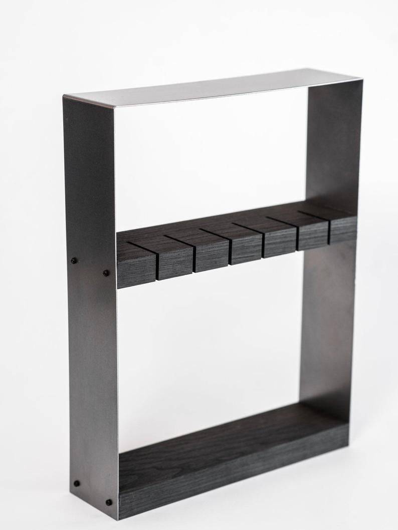 Angled view of an industrial-style knife holder featuring a dark wood block and a rugged matte black metal frame, with precision-cut horizontal slots for knife storage, set against a white background.