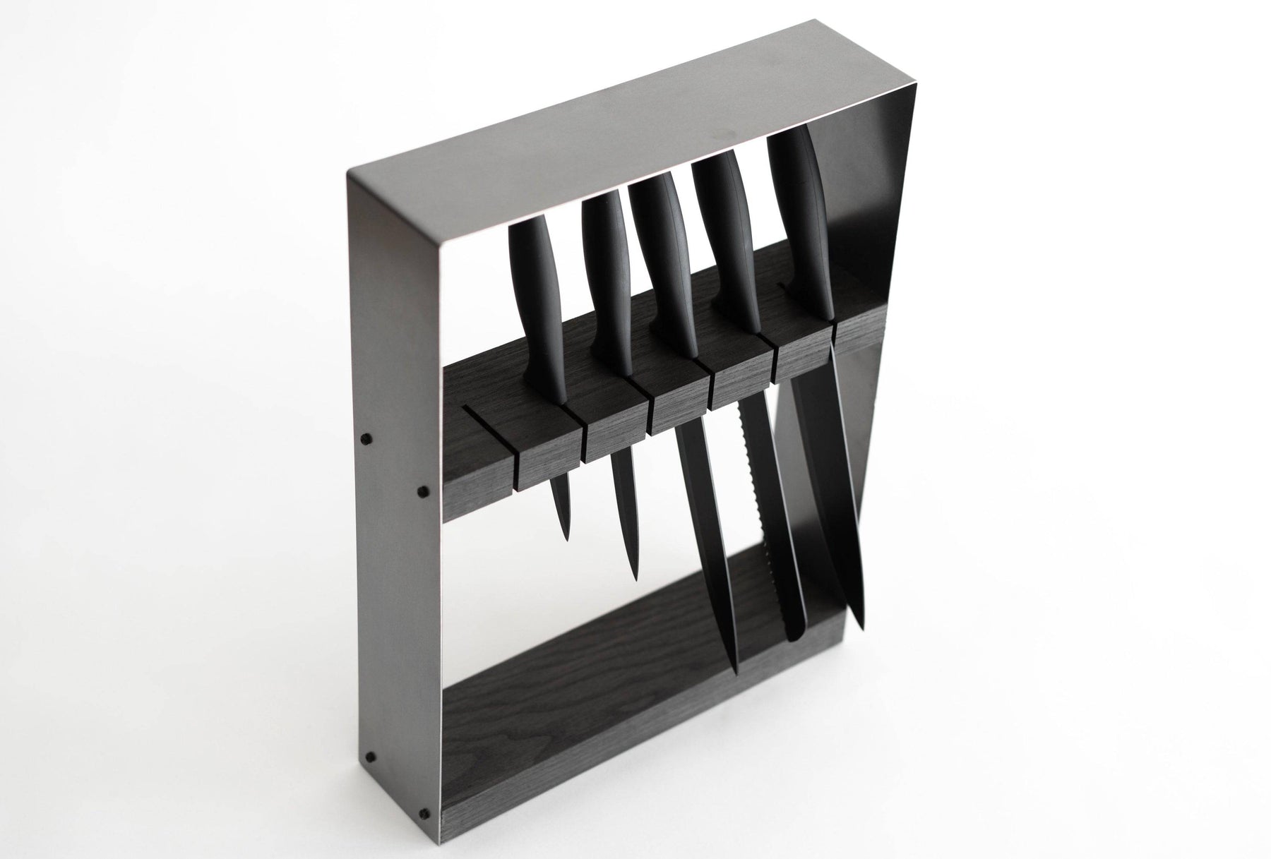 Angled view of a minimalist black knife block with a dark wooden top and metal frame, holding six black-handled knives in horizontal slots, displayed against a white background.