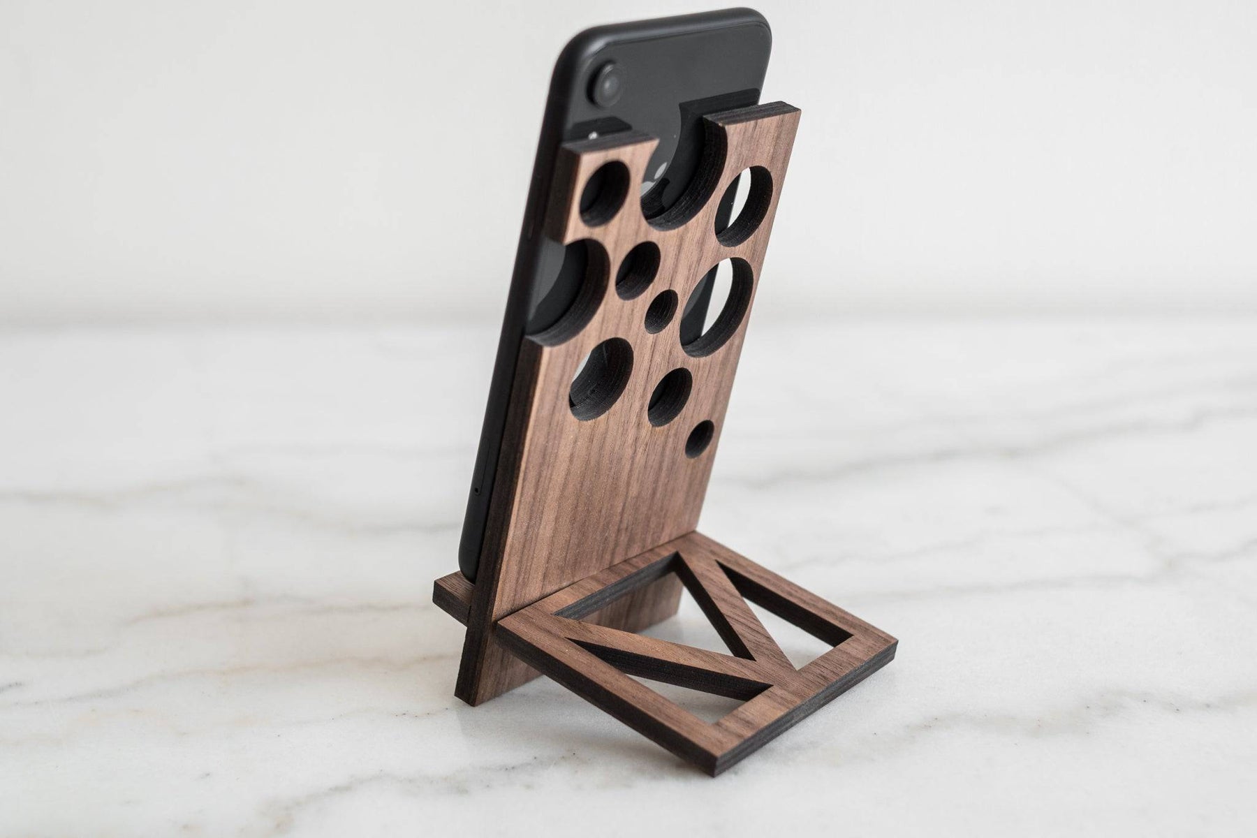 Wooden phone stand with a unique geometric design featuring circular cutouts, holding a phone at an angle on a smooth surface.