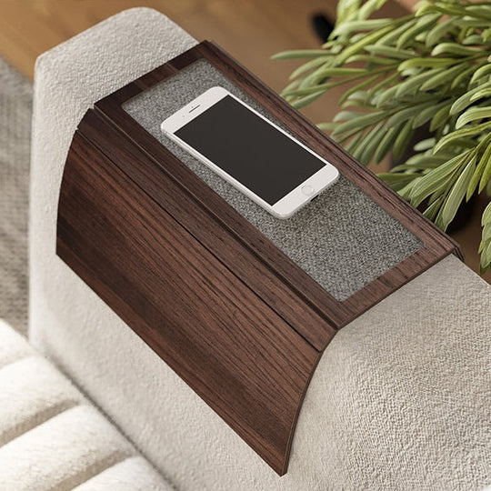 Elegant dark wood armrest tray with gray fabric detailing, resting on a beige sofa and holding a white smartphone.