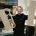 A smiling craftsman in a workshop holds two wooden pieces of the toy bus frame, showcasing his skilled craftsmanship.