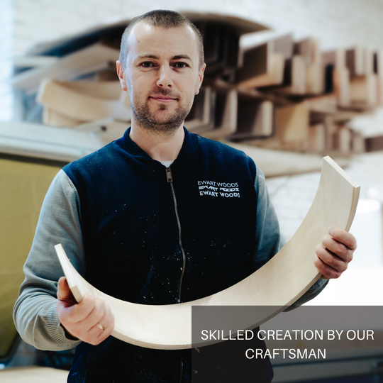 A craftsman from EWART WOODS holding a curved piece of wood, showcasing skilled craftsmanship in the workshop.