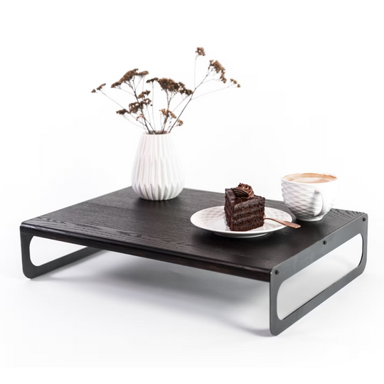 Elegant wooden serving tray with a black finish, featuring sleek metal legs. The tray is adorned with a white vase of dried flowers, a plate with a slice of cake, and a cup of coffee, all arranged neatly.