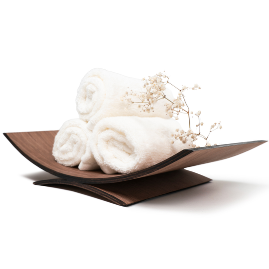 Walnut curved wooden holder with rolled white towels and decorative flowers, isolated on white.