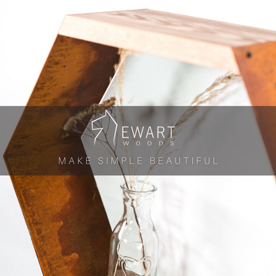 Hexagonal shelf made of rust-colored metal and natural wood, featuring a glass vase with dried plants. The Ewart Woods logo and the slogan "Make Simple Beautiful" are overlaid on a semi-transparent black strip.