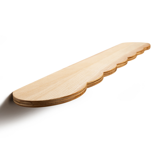 Wooden shelf with a scalloped edge design and a smooth, light wood finish, mounted on a wall and viewed from a side angle.