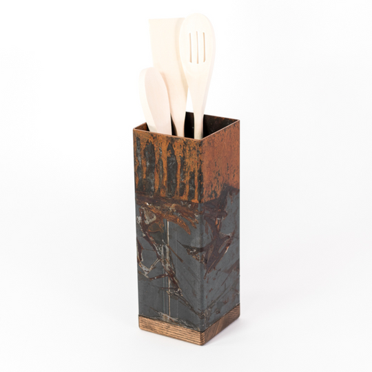 Tall, industrial-style utensil holder with a distressed metal finish and wooden base, holding wooden kitchen tools, including a spoon and spatula. The holder is displayed against a clean white background.