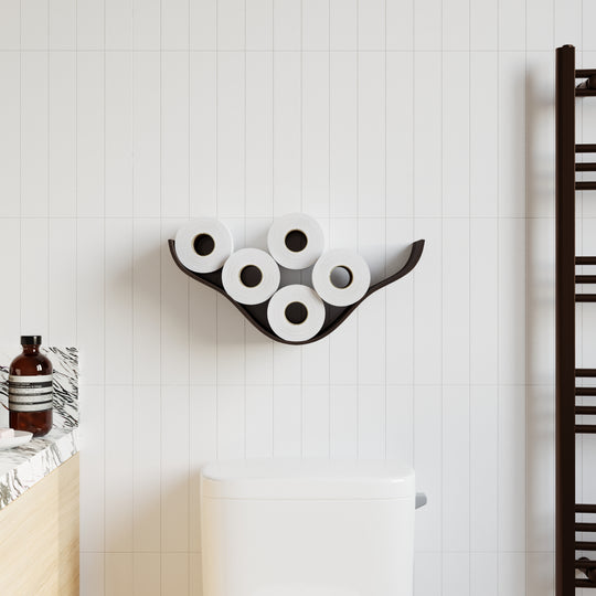 Smoked oak wooden wall shelf with a cloud-shaped, curved design holding five rolls of toilet paper, mounted on white tiled walls in a modern bathroom next to a toilet and towel rack.