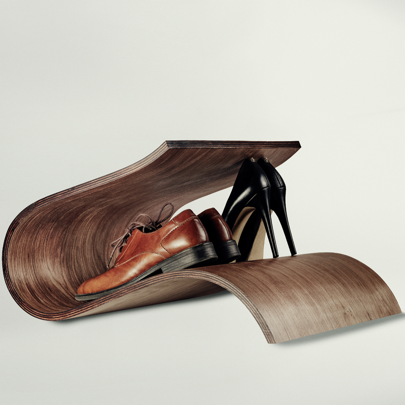 A pair of brown leather oxford shoes and a pair of black high-heeled stiletto pumps arranged inside a sculptural curved wooden display shelf on a light gray studio background.