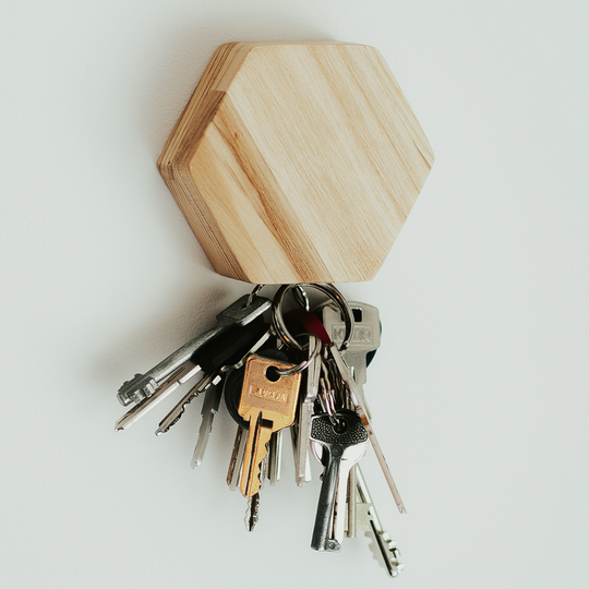 A hexagonal natural wooden key holder mounted on a wall, holding a set of metal keys on a keyring.