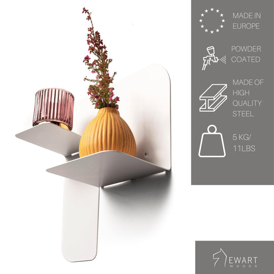 Powder-coated white floating metal organizer with a dual-level design, made from high-quality steel. Mounted securely with exposed screws, it holds a ribbed glass candle holder and an orange vase with flowers. Can support up to 5 kg.