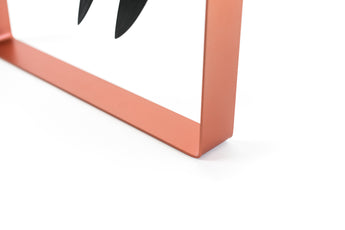 A close-up of the sleek orange metal frame of a modern knife holder, with two black-handled knives partially visible, highlighting the minimalist and contemporary design.