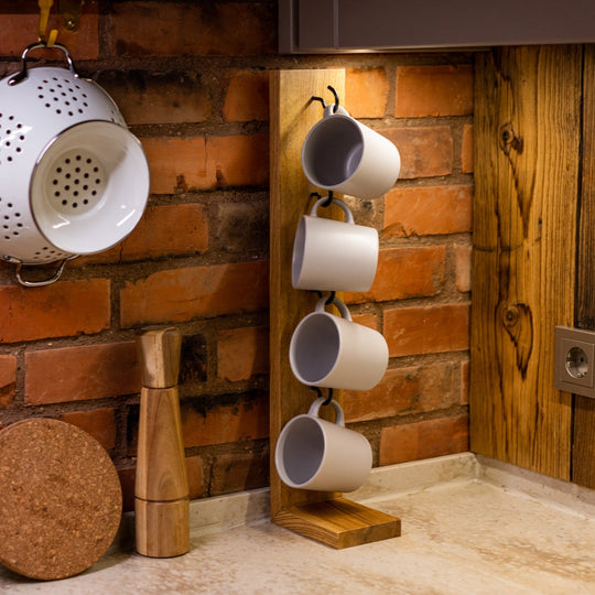 Wooden mug holder with hooks, displaying four white mugs, set on a countertop with a brick backsplash and wooden accents, creating a cozy kitchen atmosphere.