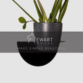 Modern black wall-mounted planter with a minimalist half-moon shape, securely holding a potted plant.