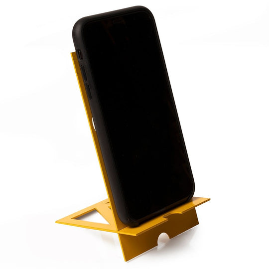 A black smartphone resting on a yellow minimalist metal phone holder with a geometric, angular design. The holder is positioned on a flat surface, showcasing its simple yet functional structure.