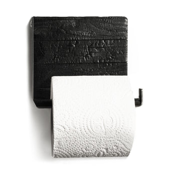 Close-up of a wall-mounted toilet paper holder featuring burned wood with a textured finish and a sleek metal bar holding a roll of toilet paper.