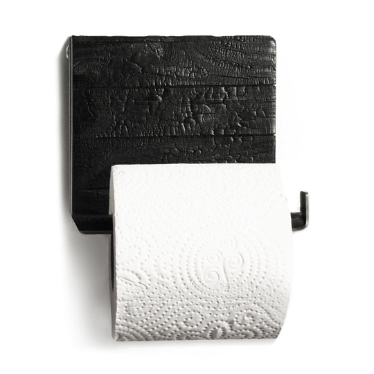 Close-up of a wall-mounted toilet paper holder featuring burned wood with a textured finish and a sleek metal bar holding a roll of toilet paper.