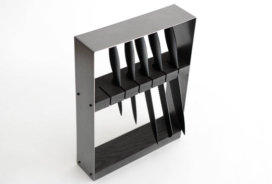 Angled view of a sleek, modern knife block featuring a black metal frame and dark wooden insert, holding six black-handled knives in evenly spaced horizontal slots.