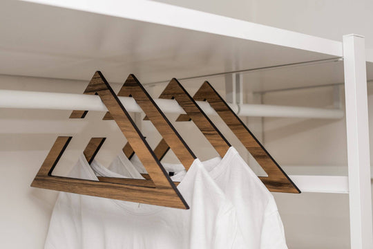 Stylish wooden hangers with a geometric triangular design, showcasing a rich paldau  finish. The hangers hold white t-shirts in a minimalist closet setup.