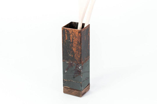 Tall, rectangular utensil holder with a rustic copper finish and wooden base, holding a pair of wooden utensils. The holder is displayed against a plain white background.