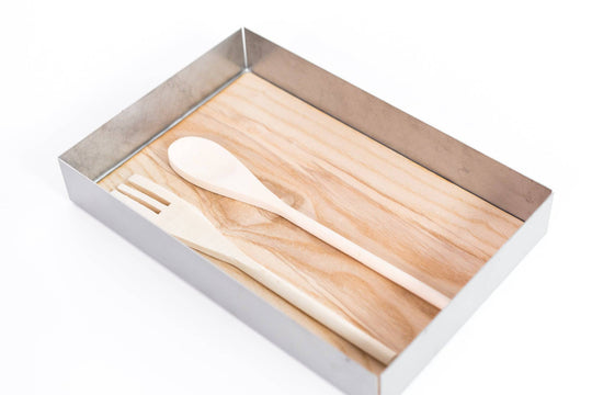 Metal container with a smooth wooden base, holding a wooden spoon and fork placed side by side.
