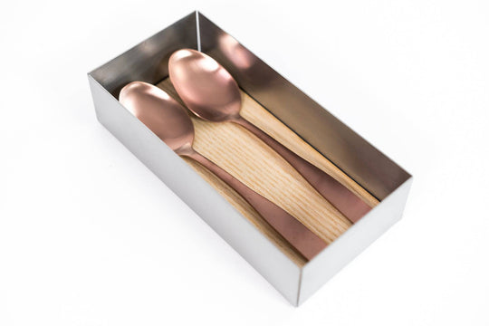 Rectangular metal container with a wooden base, holding two large copper-colored spoons neatly arranged