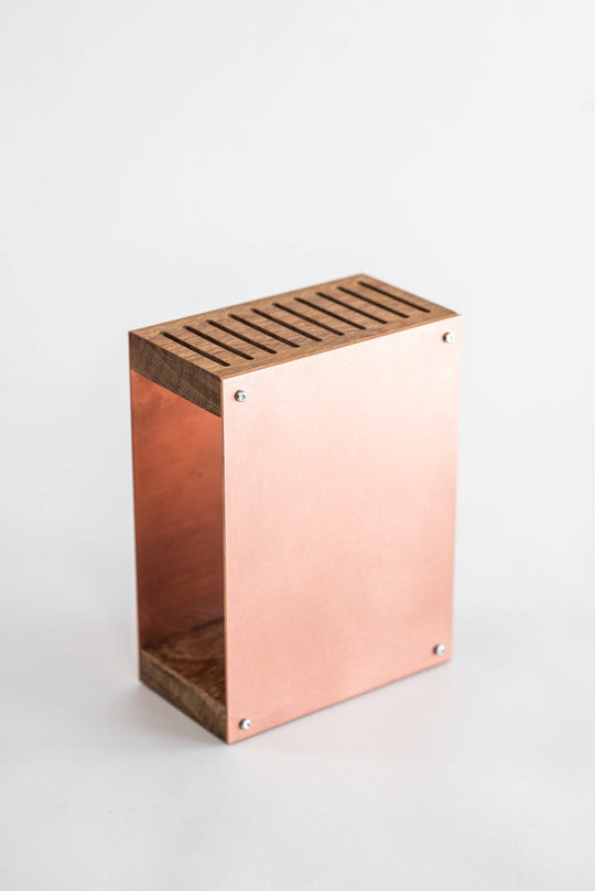 Rose gold knife block with a smooth metal finish, featuring a wooden top and base. The block has a modern, minimalist design and is displayed against a plain white background.