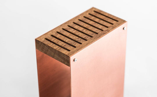 Rose gold knife block with a smooth metal exterior, wooden top. The block has a sleek, minimalist design and is displayed against a plain white background.