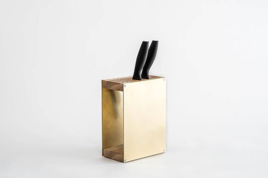 Gold-colored knife block with a smooth metal finish, wooden top and base, holding two black-handled knives. The block is displayed against a plain white background.