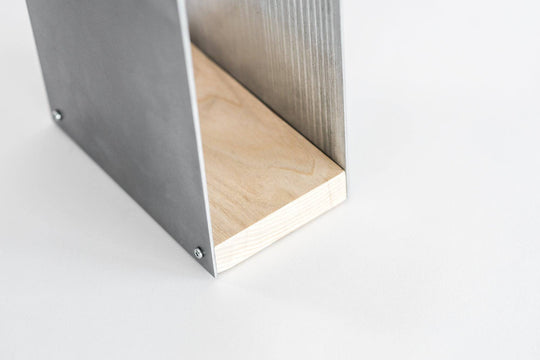 Close-up of a metal knife block with a smooth silver finish and a natural wood base. The block is displayed against a plain white background, showing the wooden grain detail at the bottom.