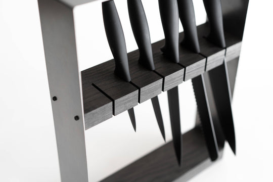 Close-up of a modern knife organizer with a dark wooden block, securing multiple black-handled knives horizontally in precision-cut slots.