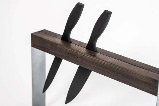 Close-up of a minimalist knife stand featuring a dark wooden block and a sleek silver metal frame, holding two black-handled knives in a single groove.