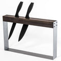 A modern, minimalist knife holder with two black-handled knives inserted vertically into a rectangular wooden and metal frame, designed for easy access and storage.