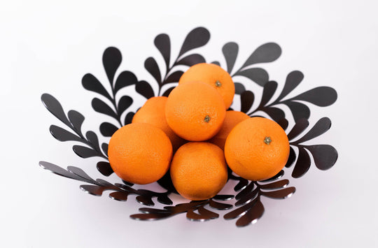 Modern black metal decorative bowl with botanical cutouts in an industrial style, holding bright orange fruits. 
