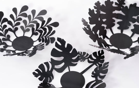 Set of three black metal decorative bowls in modern industrial style, featuring botanical cutout designs of leaves and plants.