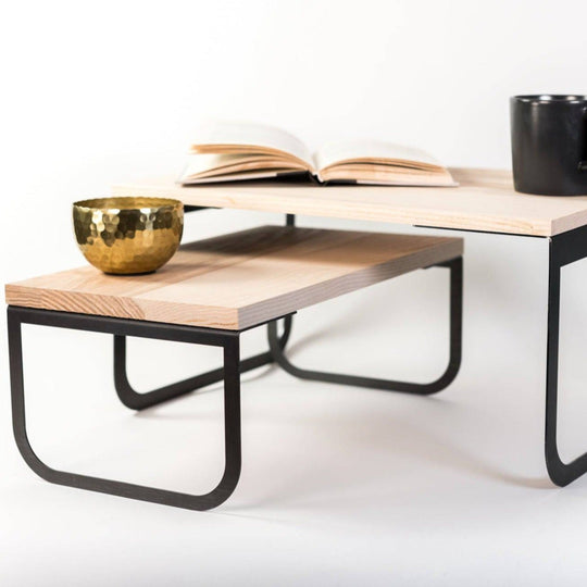 Modern wooden coffee table with black metal legs, featuring an open book, a gold bowl, and a black mug on its surface, isolated on a white background.