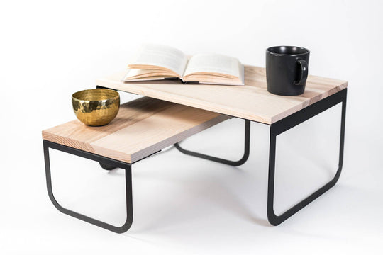 Industrial-style two-level side table with wood shelves and a black metal frame, holding a book, coffee cup, and decorative bowl.