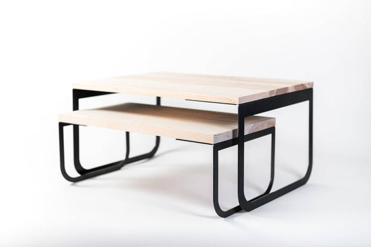 Modern dual-tier coffee table with a minimalist design, featuring natural wood surfaces and sleek black metal legs, photographed against a white background.