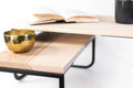 Close-up of a contemporary home decor piece: an industrial-style wood and metal side table with two levels, featuring a gold bowl and an open book.