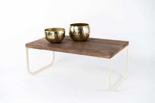 Wooden tray with light-colored metal legs, featuring two gold-toned hammered bowls on top, set against a white background.