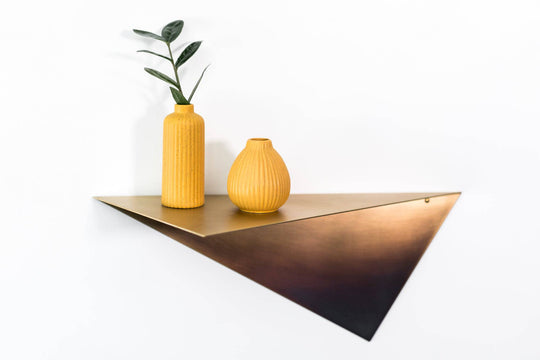Brushed copper triangular wall shelf, elegantly displaying two textured orange vases and a plant, creating a minimalist and modern look.