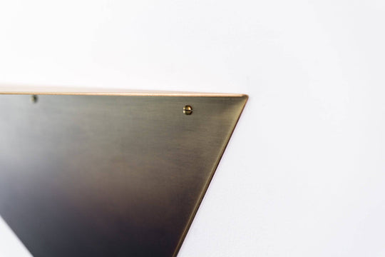 Modern triangular wall shelf with a sleek copper finish, featuring a minimalist design and visible mounting screws for easy installation.