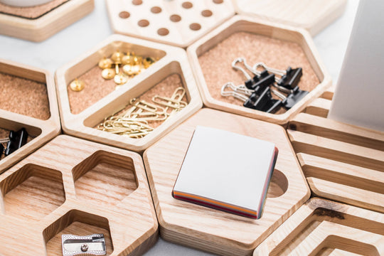 Hexagonal cork inlay organizers with wooden compartments, holding office supplies such as paper clips, thumbtacks, binder clips, and sticky notes. A modular and stylish desk accessory for organized workspaces.