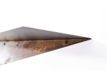 Minimalist metal shelf with a smooth surface, holding two potted cacti and a white book. The shelf has a contrasting oxidized metal edge, set against a white wall.