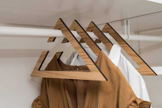 Wooden hangers in paldau finish with a geometric design, holding a brown dress and a white shirt in a closet.