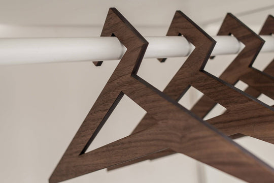 Wooden hangers in walnut finish with a smooth, textured surface and geometric triangular design, hanging on a closet rod.